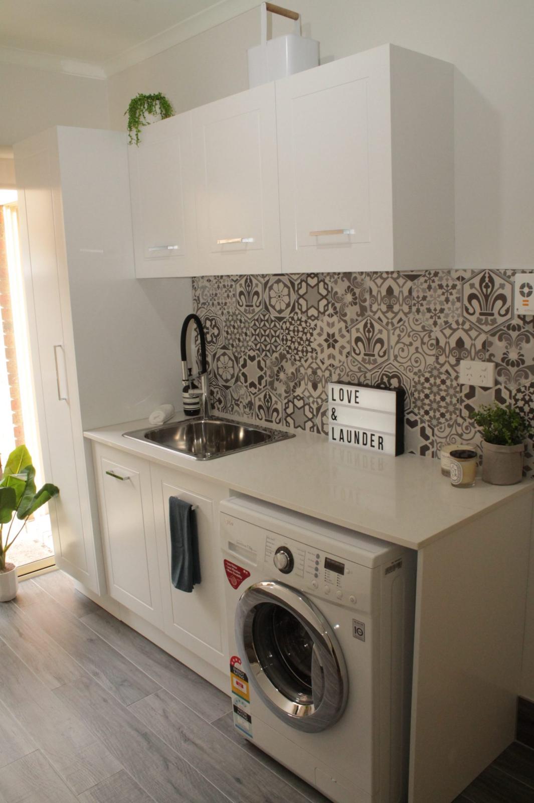 Compact modern laundry with white cabinetry, front-load washer and patterned splashback tiles