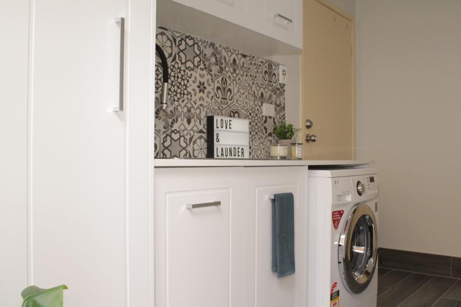 Compact white laundry with built-in cabinetry, benchtop and front-loading washing machine