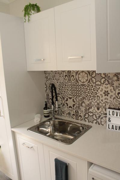 Compact white laundry with stainless steel sink and patterned tile splashback