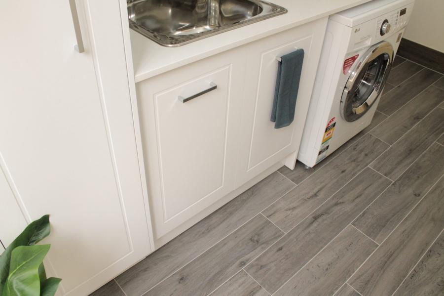 Compact white laundry cabinetry with built-in sink, washing machine and grey floor tiles
