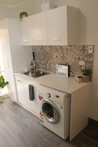 Compact white laundry renovation with washer, overhead cabinets and patterned tiled splashback