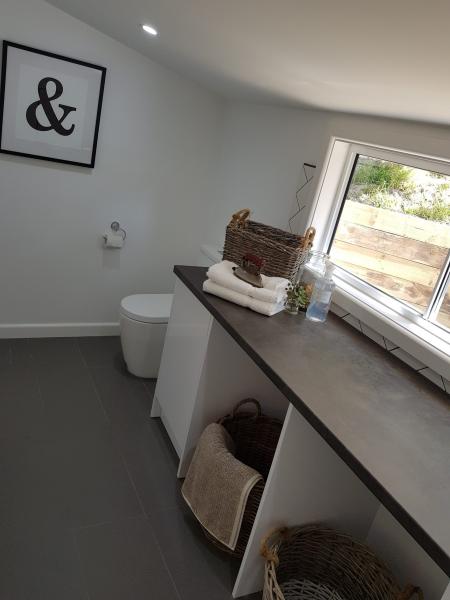Modern bathroom shelf with wicker baskets, folded towels and a sloped window beside a toilet