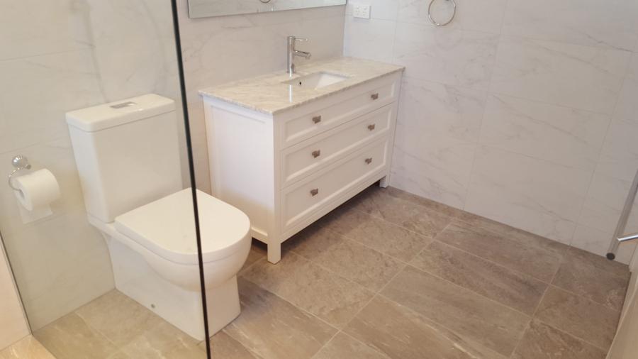 Modern white bathroom vanity and toilet with frameless glass shower screen