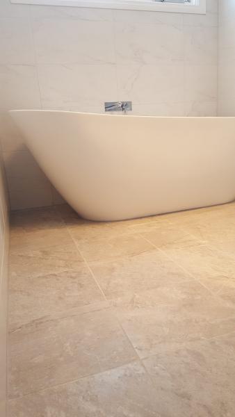 Freestanding white bath in a modern bathroom with beige floor and wall tiles