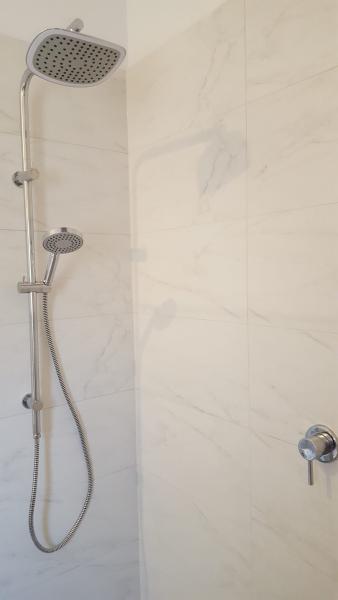 Modern shower with chrome rain shower head and handheld spray on white tiled wall