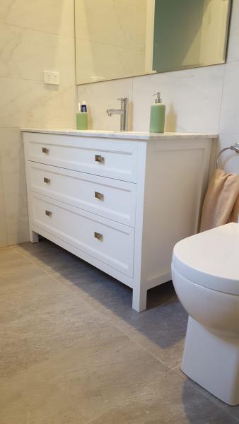 White bathroom vanity with drawers, stone top, mirror and toilet in a modern bathroom