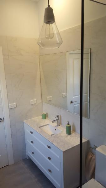 Bright bathroom vanity with marble-look walls, mirror cabinet and glass shower screen