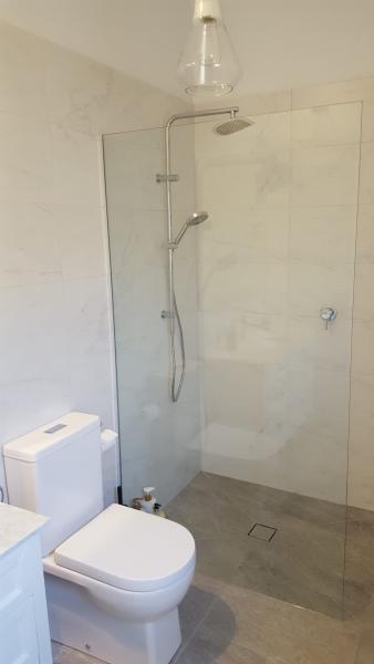 Modern bathroom with frameless glass shower, toilet and light stone tiles
