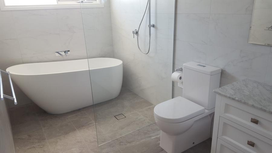 Modern white bathroom with freestanding bath, toilet and vanity in marble-look tiles