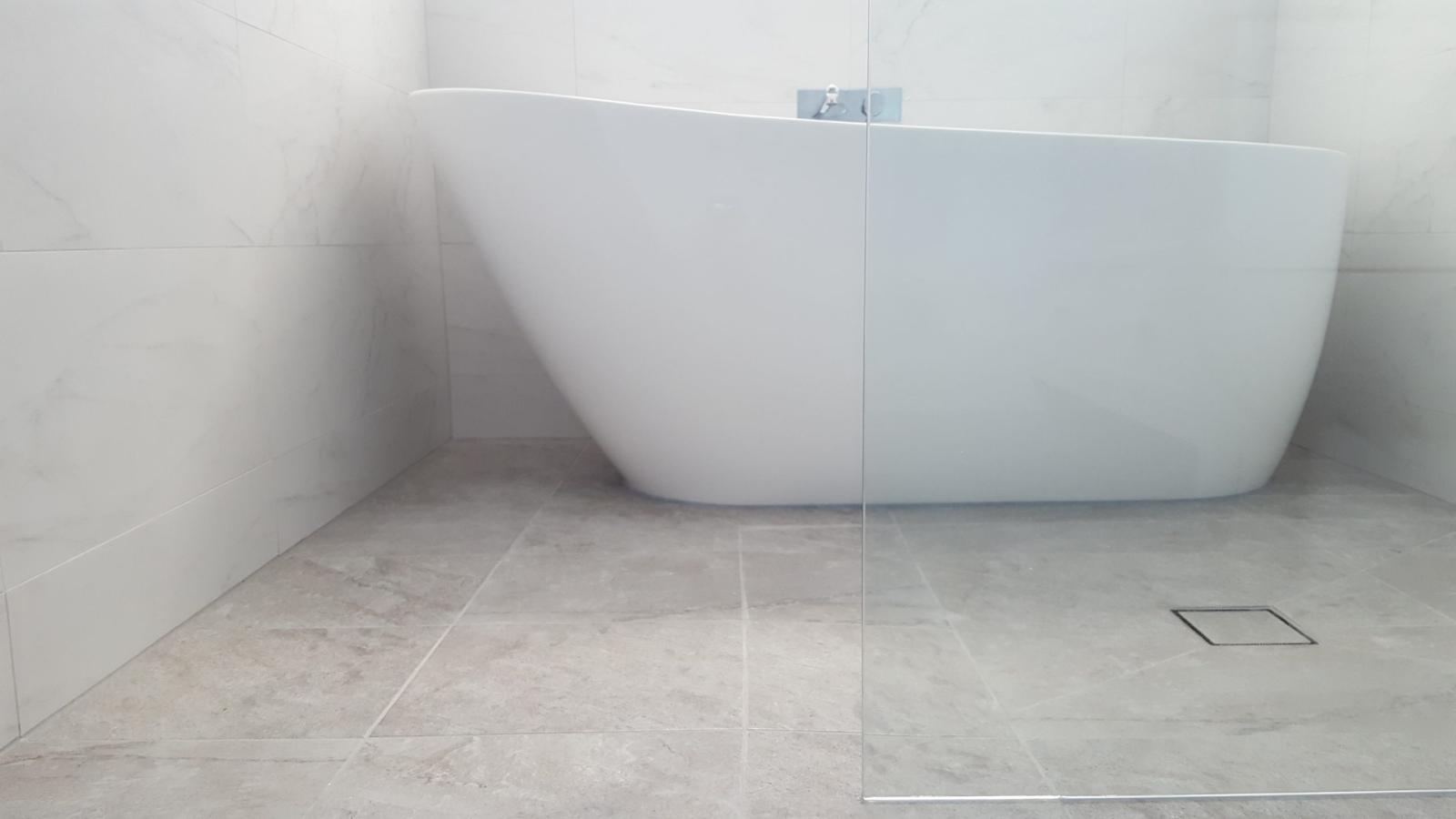 Freestanding white bath on light tiled floor in a modern minimalist bathroom