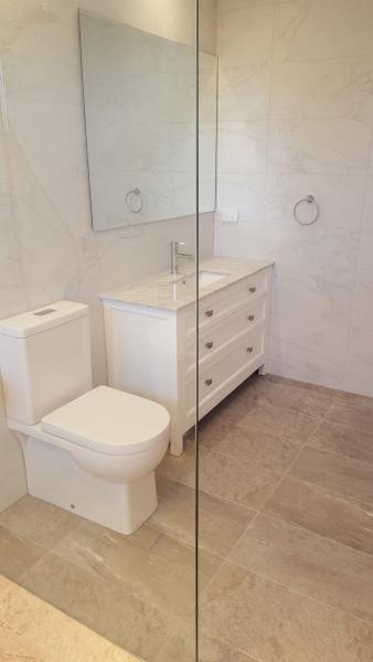 Modern white bathroom with wall-hung toilet, vanity drawers and frameless glass shower screen