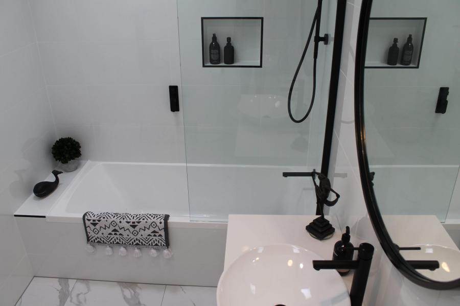 Modern white bathroom with bath, frameless shower screen and black tapware
