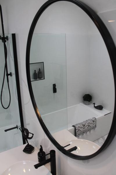 Oval black-framed bathroom mirror above a white basin with matte black tapware