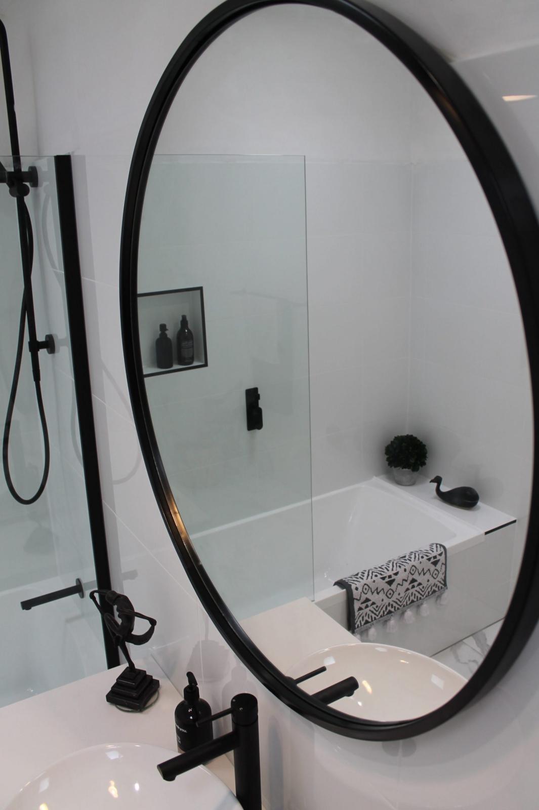 Oval black-framed bathroom mirror above a white basin with matte black tapware