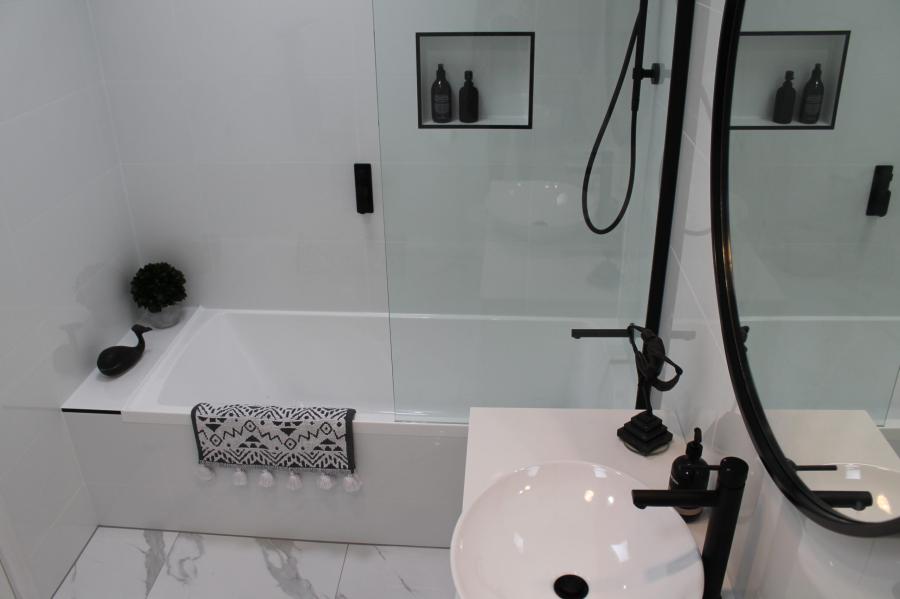 Modern white bathroom with bathtub, frameless shower screen and black tapware