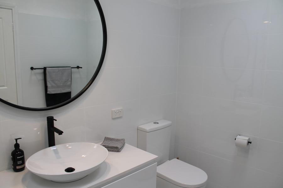 Modern white bathroom vanity with round basin, black tapware, mirror and toilet