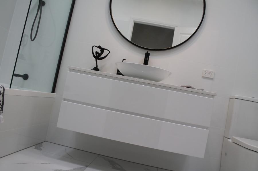 Modern white bathroom with floating vanity, round mirror and bath beside shower screen