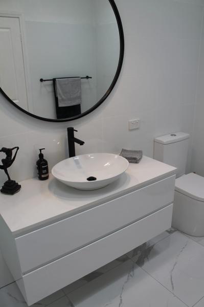 Modern white bathroom vanity with round mirror, black tapware and vessel basin beside a toilet