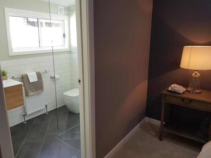 View through doorway into a modern bathroom with glass shower, timber vanity and grey floor tiles