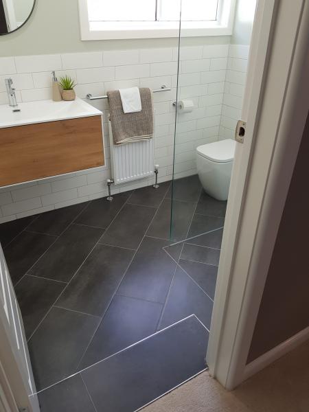 Modern bathroom with floating timber vanity, dark floor tiles and glass shower screen