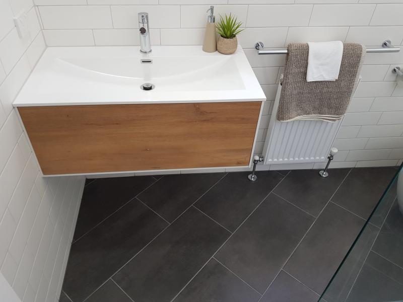 Floating timber vanity with white basin, towel rail and dark floor tiles in a modern bathroom