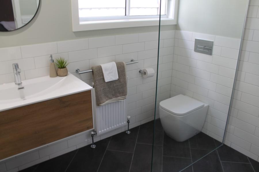 Modern white bathroom with timber vanity, wall-hung toilet and glass shower screen