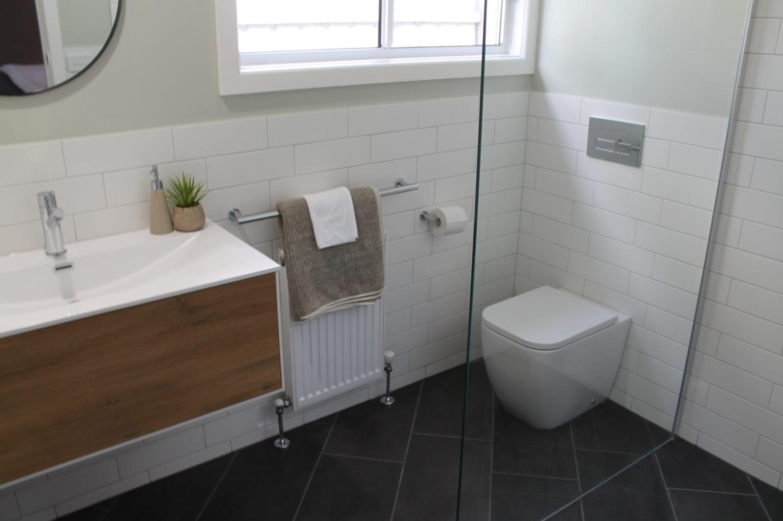 Modern white bathroom with timber vanity, wall-hung toilet and glass shower screen