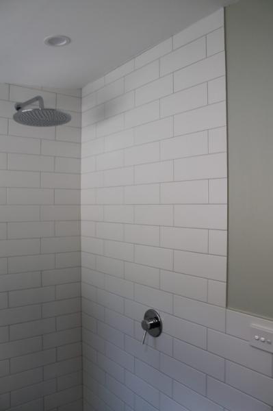 White tiled shower with chrome shower head and mixer in a modern bathroom