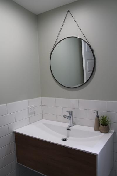 Round mirror above vanity basin in a modern bathroom with white wall tiles