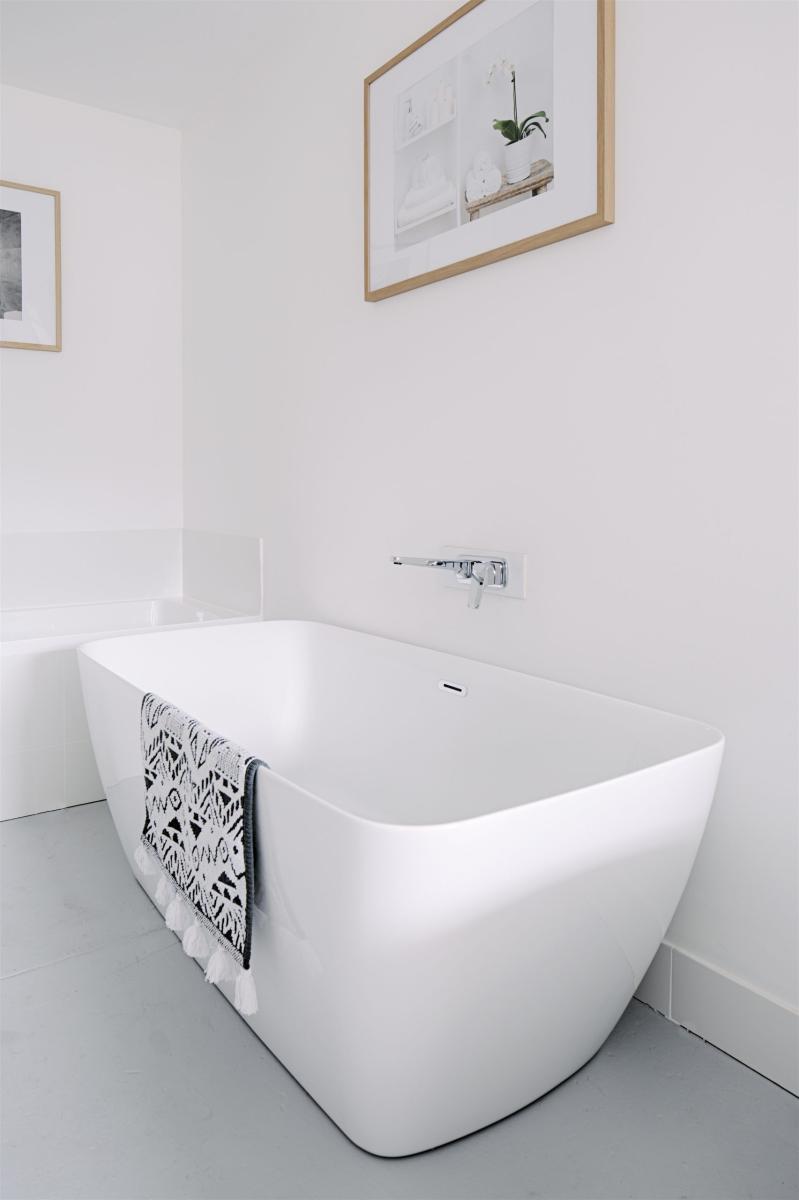 Freestanding white bathtub in a minimalist modern bathroom with framed wall art