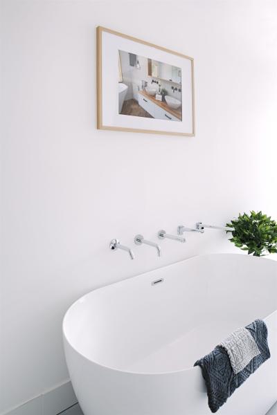 Freestanding white bathtub with wall-mounted tapware and framed bathroom artwork
