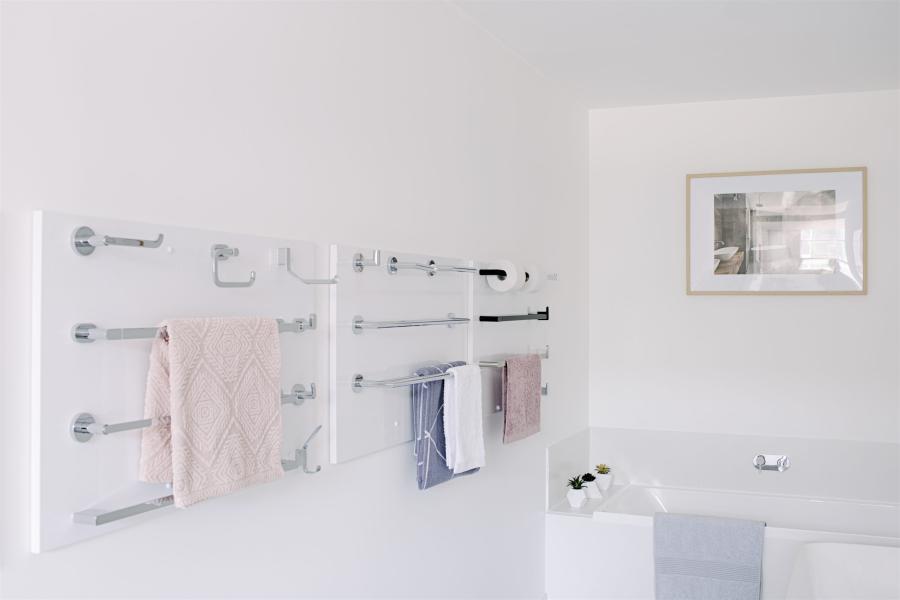 Bright white bathroom with chrome towel rails, pale towels and framed wall art