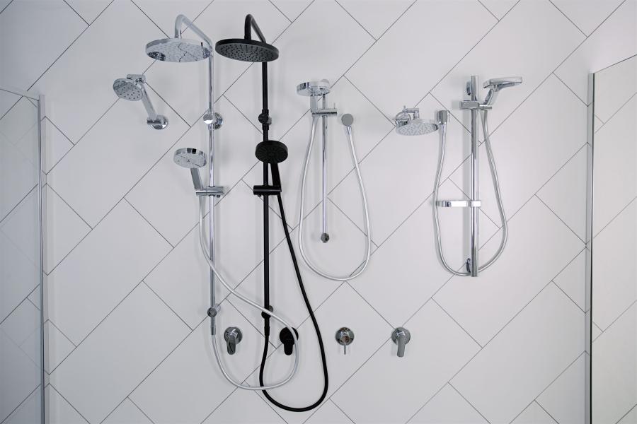 Wall-mounted shower fittings on white herringbone tiles in a modern bathroom display