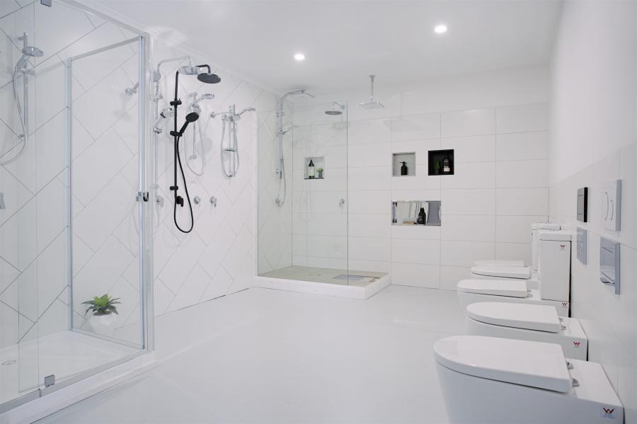 Spacious all-white modern bathroom with walk-in showers, wall-hung toilets and folded towels