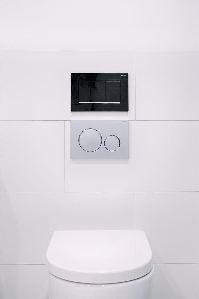Wall-hung toilet with concealed cistern and dual flush plate on white tiled bathroom wall