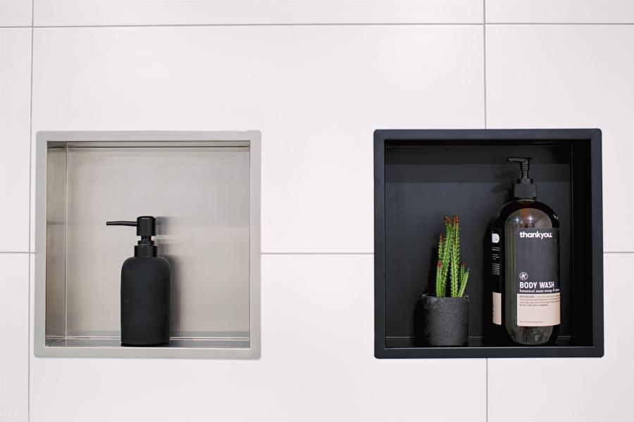Two recessed shower niches in a tiled bathroom wall with bottles and a small plant