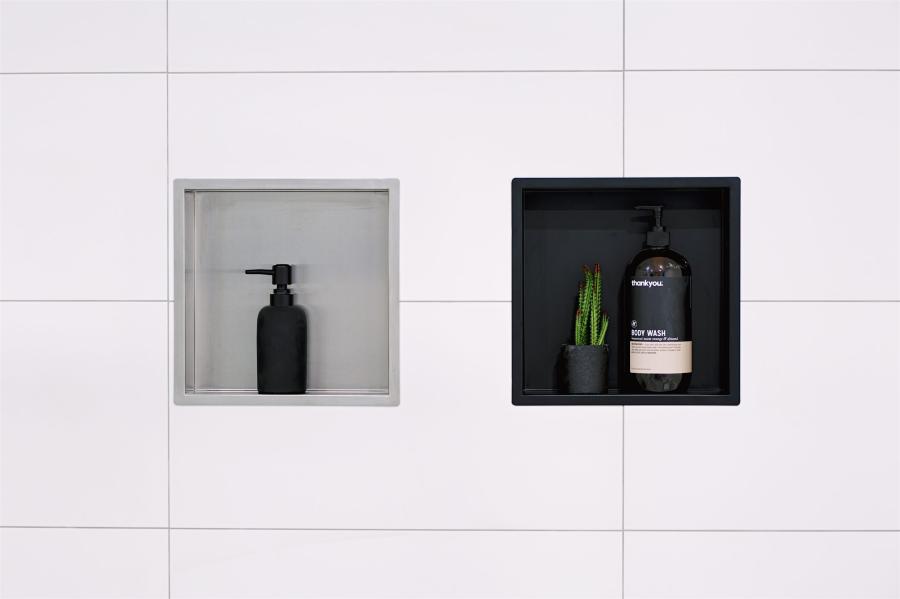Two recessed bathroom wall niches in white tiled shower wall, one white and one black, styled with bottles