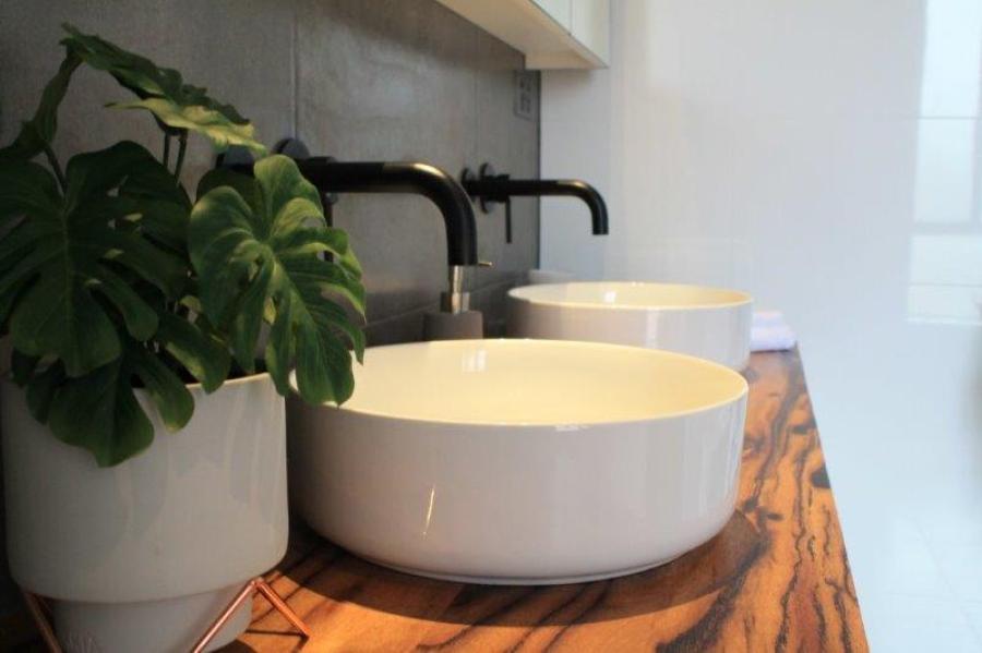 Round white vessel basin on timber vanity with black tapware and indoor plant