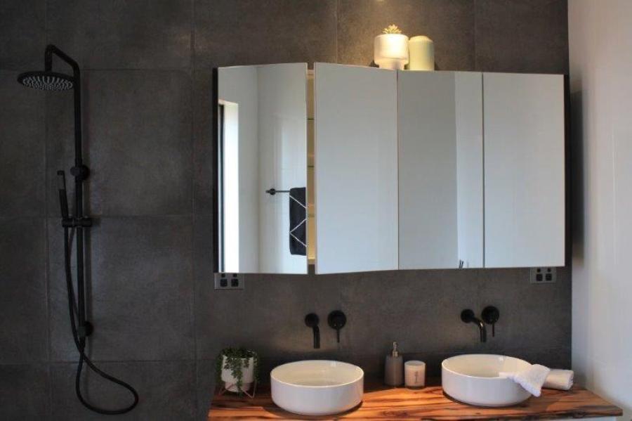 Modern bathroom vanity with double basins, mirrored cabinets and black shower set against dark grey tiles