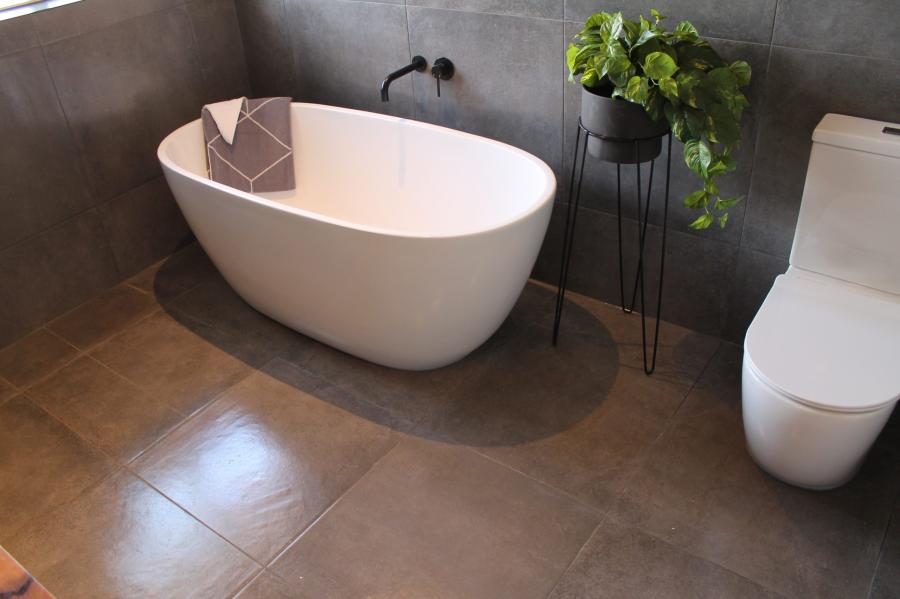 Modern freestanding white bath beside toilet in a grey tiled bathroom