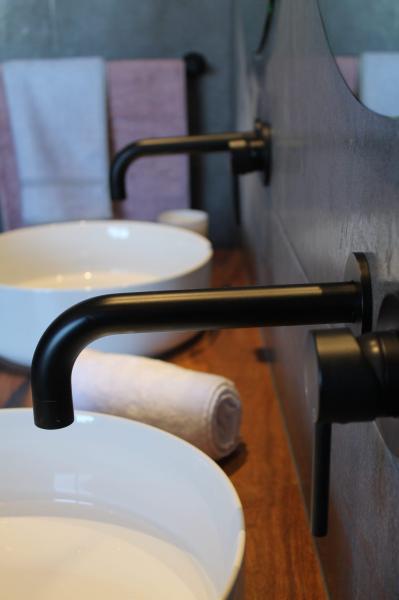 Matte black wall-mounted tapware above white vessel basins on a timber vanity
