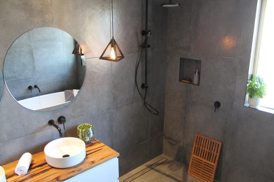 Modern grey tiled bathroom with walk-in shower, timber vanity top and round mirror