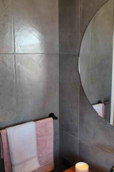 Grey tiled bathroom wall with round mirror and blush pink towels