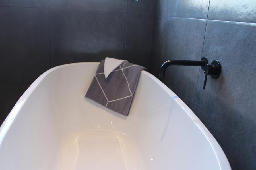Freestanding white bath with black wall tapware against dark grey bathroom tiles