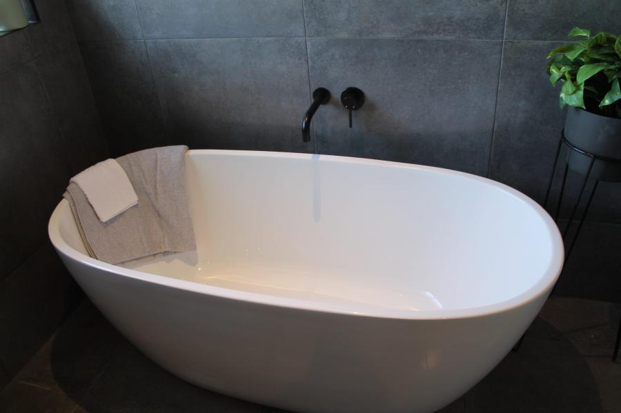 Freestanding white bath against dark grey tiled bathroom wall
