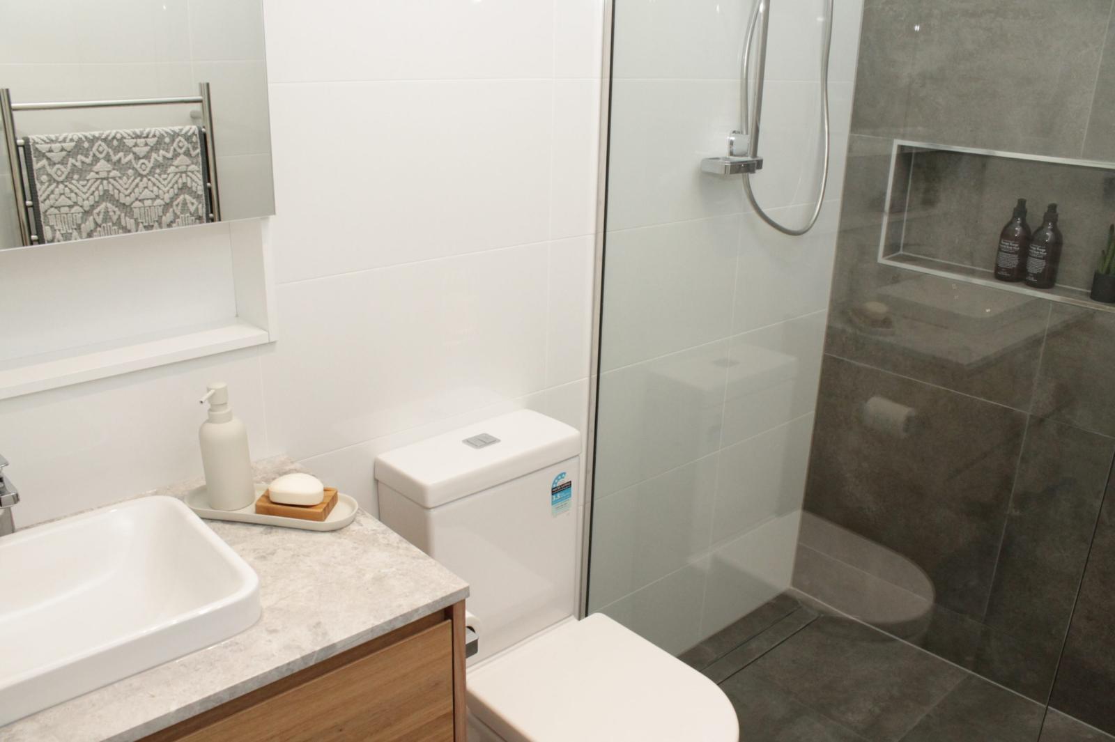 Modern bathroom with vanity, toilet and glass shower with tiled niche