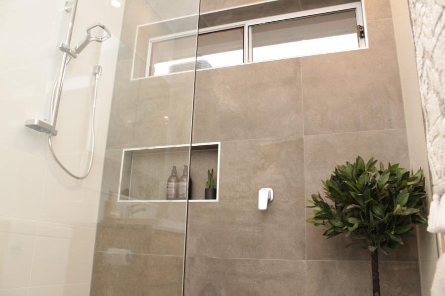 Modern tiled shower with glass screen, recessed niche and high window