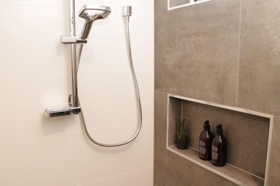 Handheld shower beside recessed tiled niche with bottles in a modern bathroom