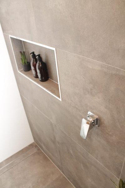 Tiled shower wall with recessed niche and chrome mixer in a modern bathroom
