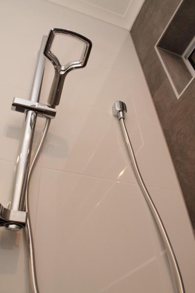 Chrome handheld shower on white tiled wall in a modern bathroom